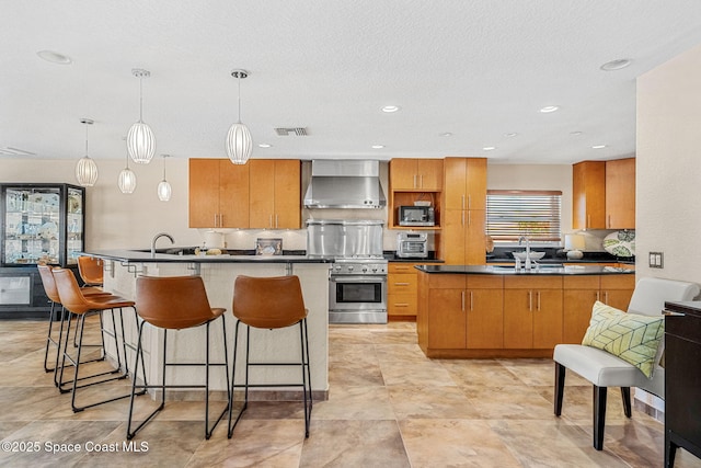 kitchen with sink, hanging light fixtures, wall chimney exhaust hood, and appliances with stainless steel finishes