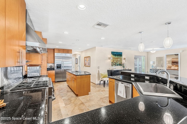 kitchen featuring extractor fan, sink, hanging light fixtures, stainless steel appliances, and a center island with sink