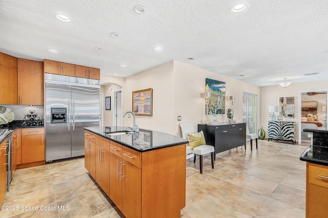 kitchen featuring built in refrigerator, sink, a center island with sink, and a textured ceiling