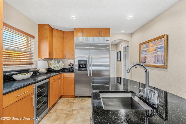 kitchen with sink, dark stone countertops, wine cooler, built in refrigerator, and a textured ceiling