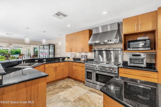 kitchen with sink, appliances with stainless steel finishes, hanging light fixtures, kitchen peninsula, and wall chimney exhaust hood