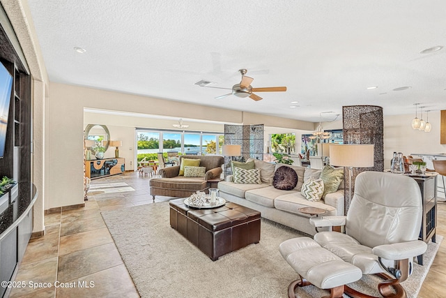 living room featuring ceiling fan with notable chandelier and a textured ceiling