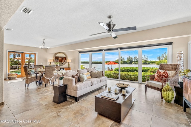 tiled living room featuring a textured ceiling, ceiling fan with notable chandelier, a healthy amount of sunlight, and a water view