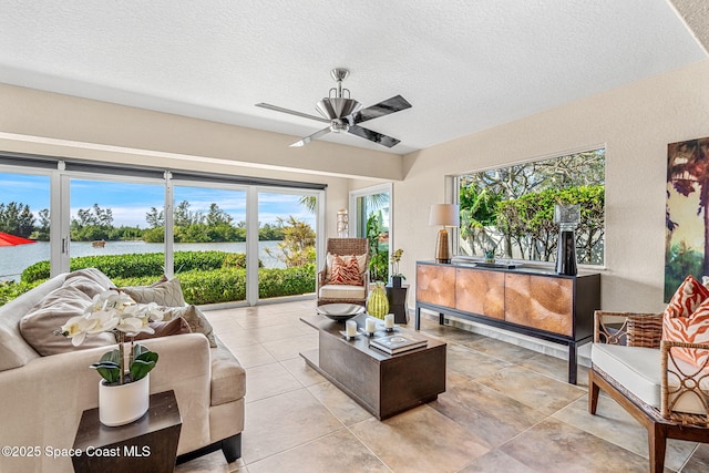 living room featuring ceiling fan, a textured ceiling, and a water view