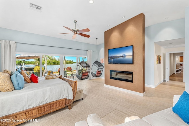 bedroom featuring a towering ceiling, a large fireplace, access to exterior, ceiling fan, and light hardwood / wood-style flooring