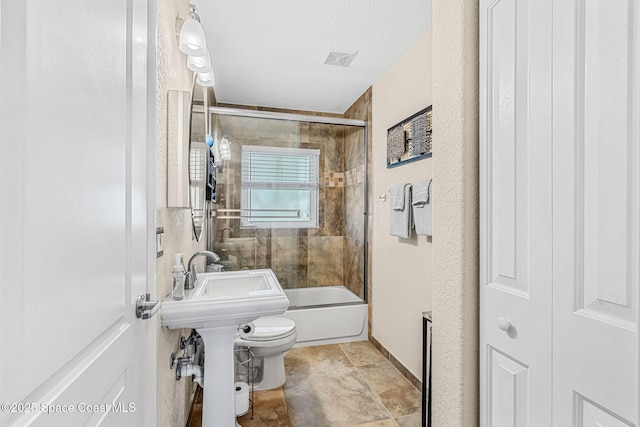 bathroom featuring a textured ceiling, enclosed tub / shower combo, and toilet