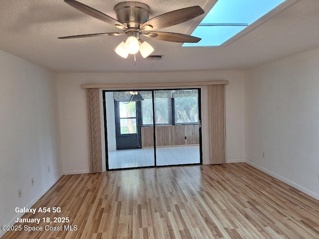 empty room with ceiling fan, a skylight, light hardwood / wood-style floors, and a textured ceiling