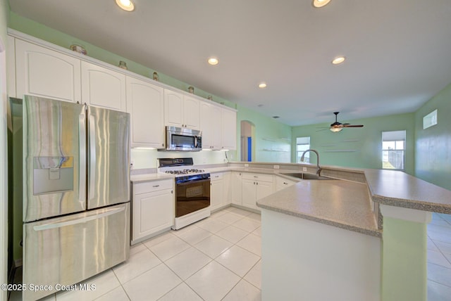 kitchen featuring light tile patterned floors, stainless steel appliances, a peninsula, a sink, and white cabinets