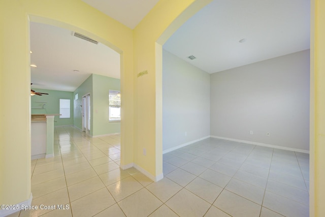 spare room with visible vents, arched walkways, a ceiling fan, baseboards, and tile patterned floors