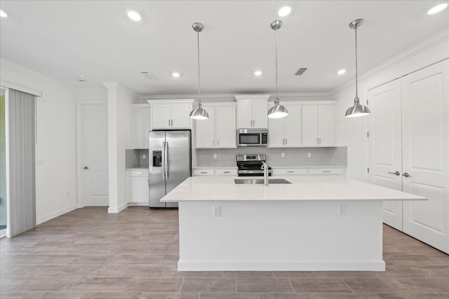 kitchen featuring decorative light fixtures, white cabinetry, a center island with sink, and stainless steel appliances