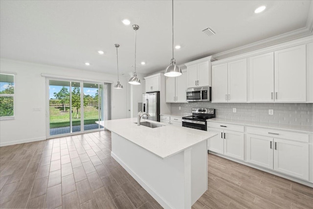 kitchen featuring decorative light fixtures, white cabinets, stainless steel appliances, and a kitchen island with sink