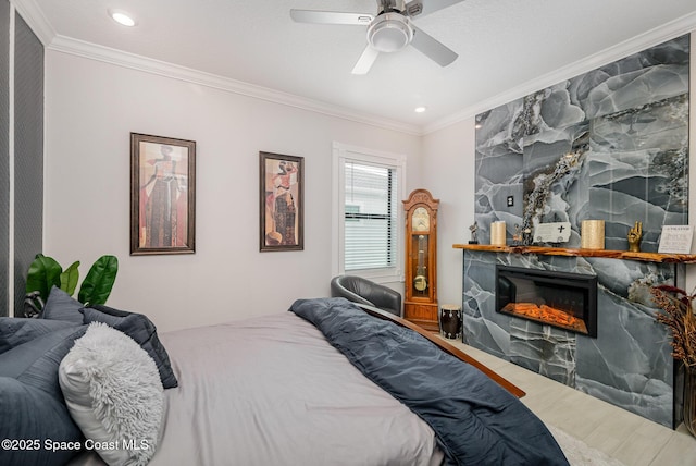 bedroom with hardwood / wood-style flooring, crown molding, ceiling fan, and a fireplace