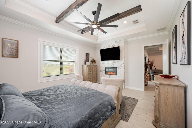 bedroom featuring crown molding, light hardwood / wood-style floors, a premium fireplace, and a raised ceiling