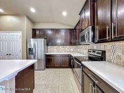 kitchen featuring vaulted ceiling, dark brown cabinetry, stainless steel appliances, and tasteful backsplash