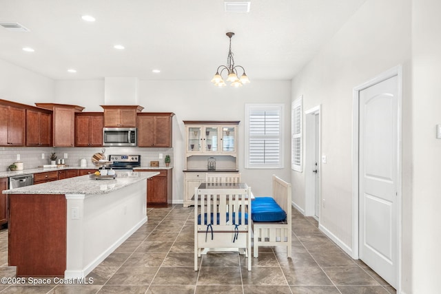 kitchen featuring tasteful backsplash, decorative light fixtures, a kitchen island, stainless steel appliances, and light stone countertops