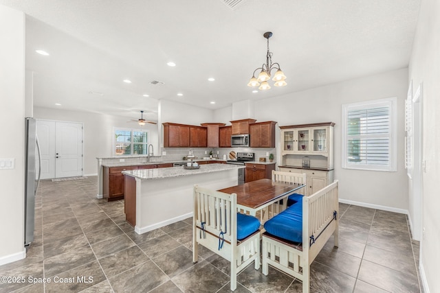 kitchen with appliances with stainless steel finishes, pendant lighting, sink, a center island, and light stone counters