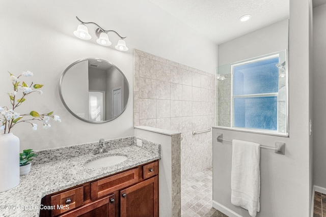 bathroom with tiled shower, vanity, and a textured ceiling