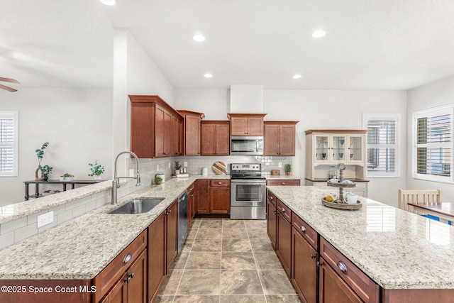 kitchen with sink, stainless steel appliances, a center island, light stone countertops, and decorative backsplash