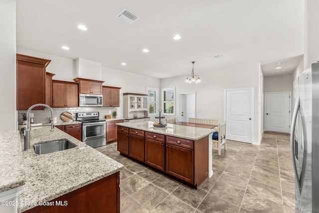 kitchen featuring appliances with stainless steel finishes, sink, hanging light fixtures, a center island, and light stone counters