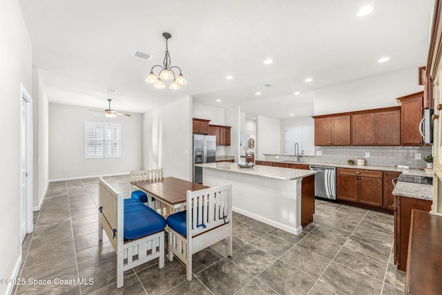 kitchen with sink, a center island, hanging light fixtures, stainless steel appliances, and light stone countertops