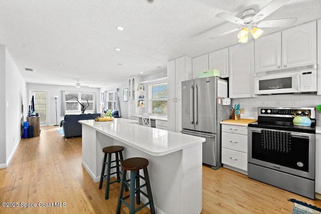 kitchen featuring light hardwood / wood-style floors, stainless steel appliances, decorative backsplash, a kitchen breakfast bar, and white cabinets