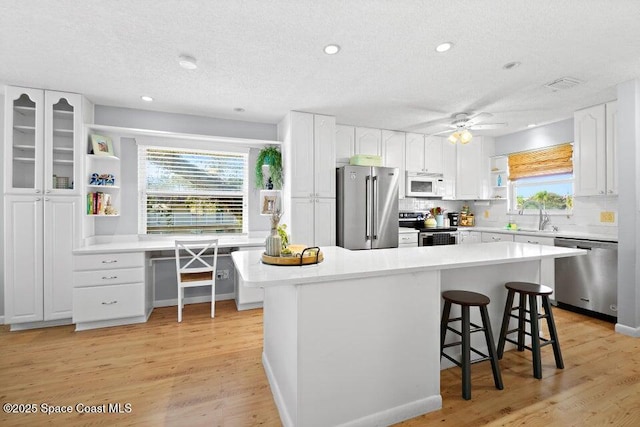 kitchen with a breakfast bar area, appliances with stainless steel finishes, a textured ceiling, a kitchen island, and white cabinets