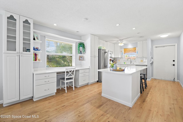 kitchen with a kitchen island, white cabinetry, stainless steel fridge, light hardwood / wood-style flooring, and a breakfast bar area