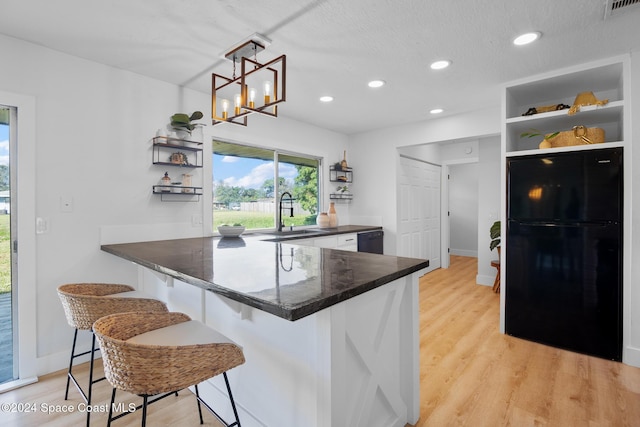 kitchen with sink, a kitchen breakfast bar, black fridge, kitchen peninsula, and light wood-type flooring