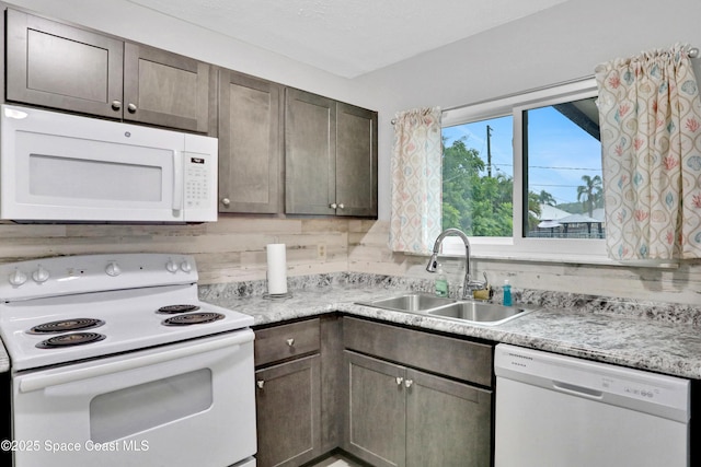 kitchen with white appliances, dark brown cabinetry, and sink