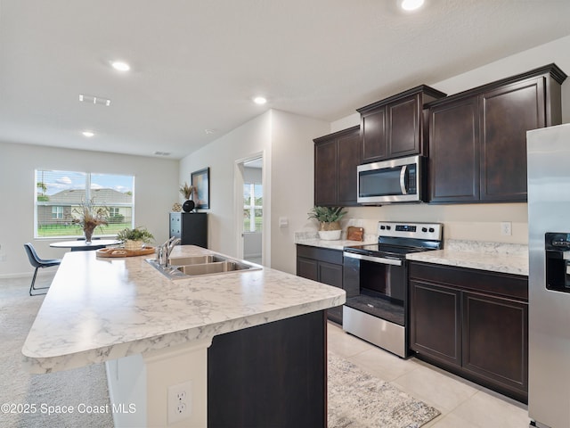 kitchen featuring sink, a kitchen island with sink, light tile patterned floors, stainless steel appliances, and dark brown cabinets