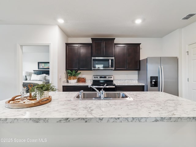 kitchen featuring appliances with stainless steel finishes, a kitchen island with sink, sink, and dark brown cabinets