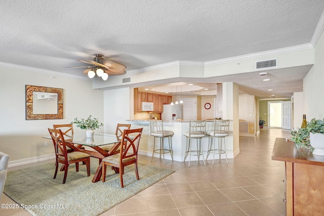 tiled dining room featuring ceiling fan, ornamental molding, and a textured ceiling