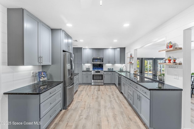 kitchen with gray cabinetry, dark stone countertops, stainless steel appliances, light hardwood / wood-style floors, and kitchen peninsula