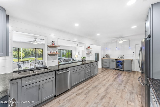 kitchen featuring sink, stainless steel appliances, wine cooler, dark stone counters, and light wood-type flooring