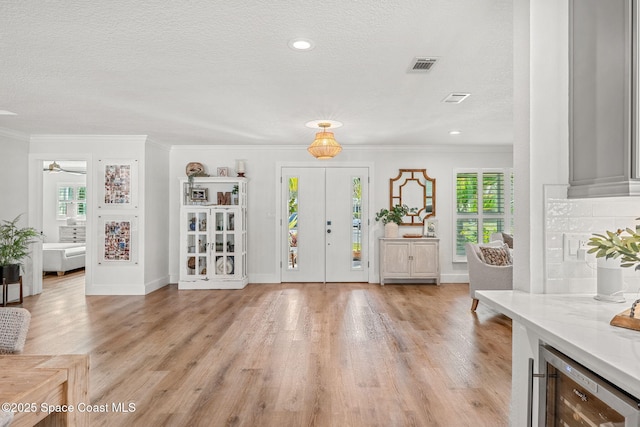 foyer entrance featuring crown molding, a textured ceiling, beverage cooler, and light hardwood / wood-style floors