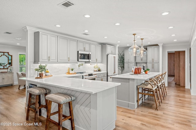 kitchen featuring high end fridge, decorative light fixtures, ornamental molding, a kitchen breakfast bar, and an island with sink