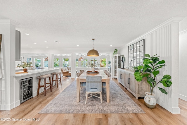 dining space featuring light hardwood / wood-style flooring, ornamental molding, beverage cooler, and a textured ceiling