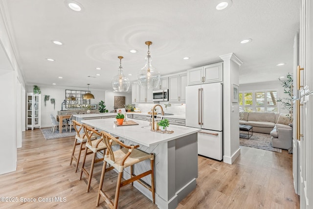 kitchen featuring a breakfast bar area, white cabinetry, light hardwood / wood-style flooring, pendant lighting, and high end white fridge