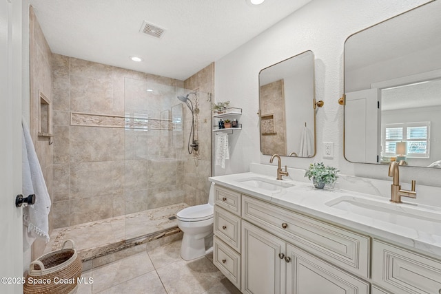 bathroom with vanity, toilet, tile patterned flooring, and a tile shower