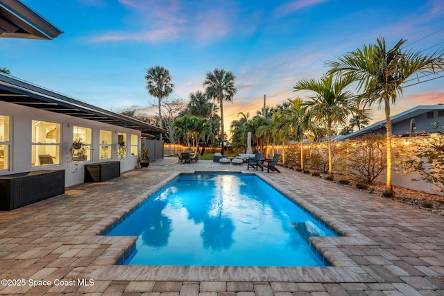 pool at dusk with outdoor lounge area and a patio area