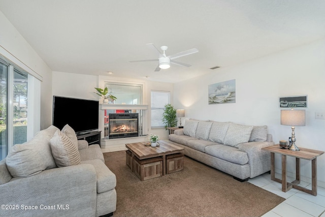 tiled living room with a tiled fireplace, ceiling fan, and a healthy amount of sunlight