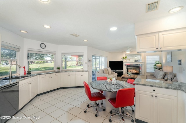 kitchen featuring sink, light tile patterned floors, white cabinetry, black dishwasher, and light stone counters