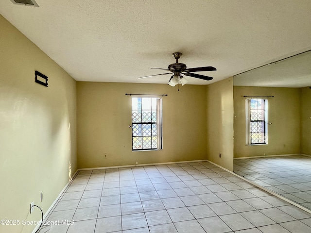 tiled spare room with a wealth of natural light, a textured ceiling, and ceiling fan