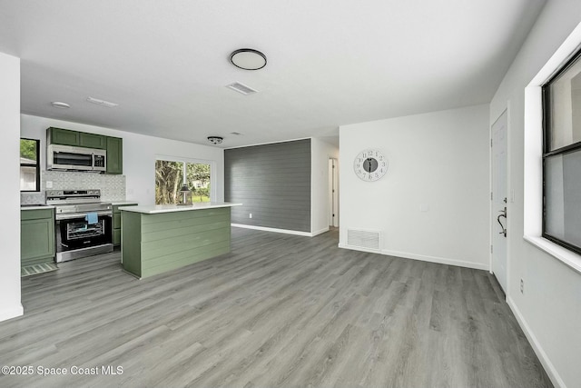 kitchen featuring appliances with stainless steel finishes, decorative backsplash, light wood-type flooring, green cabinetry, and a center island