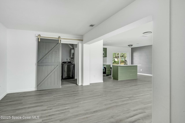 unfurnished room featuring washer / dryer, water heater, a barn door, and light hardwood / wood-style flooring