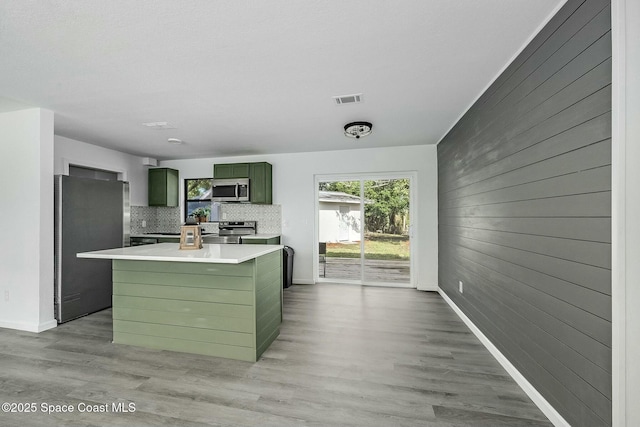 kitchen with tasteful backsplash, a kitchen island, light wood-type flooring, green cabinetry, and stainless steel appliances