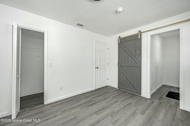 unfurnished bedroom with hardwood / wood-style flooring, a textured ceiling, a closet, and a barn door