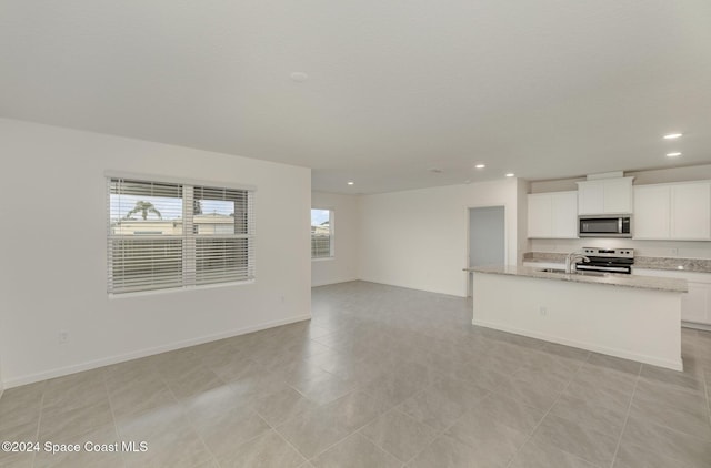 kitchen featuring a center island with sink, appliances with stainless steel finishes, light stone countertops, white cabinets, and sink