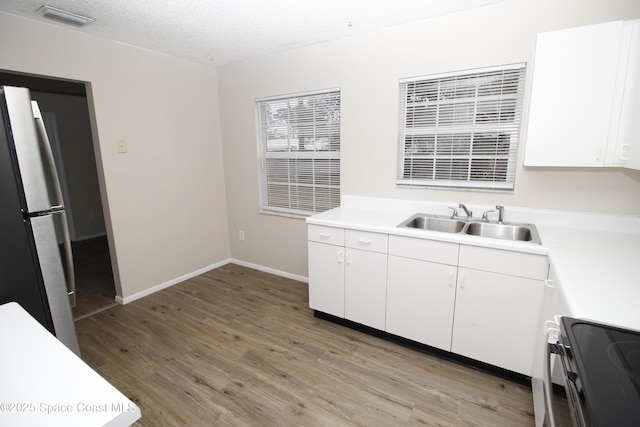 kitchen featuring a textured ceiling, white cabinets, electric stove, sink, and fridge