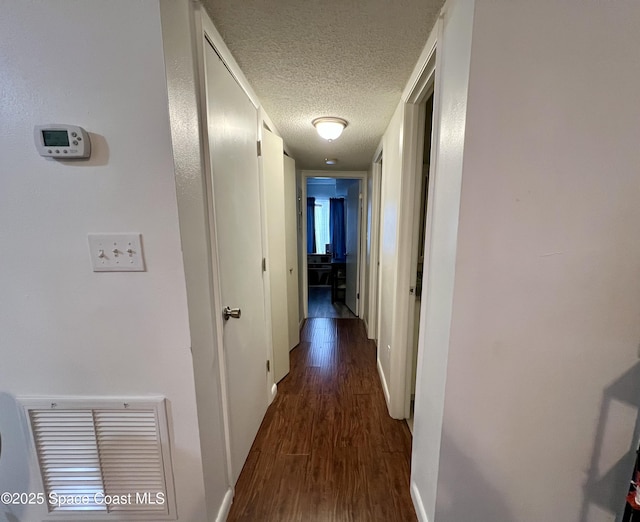 corridor with a textured ceiling and dark hardwood / wood-style flooring